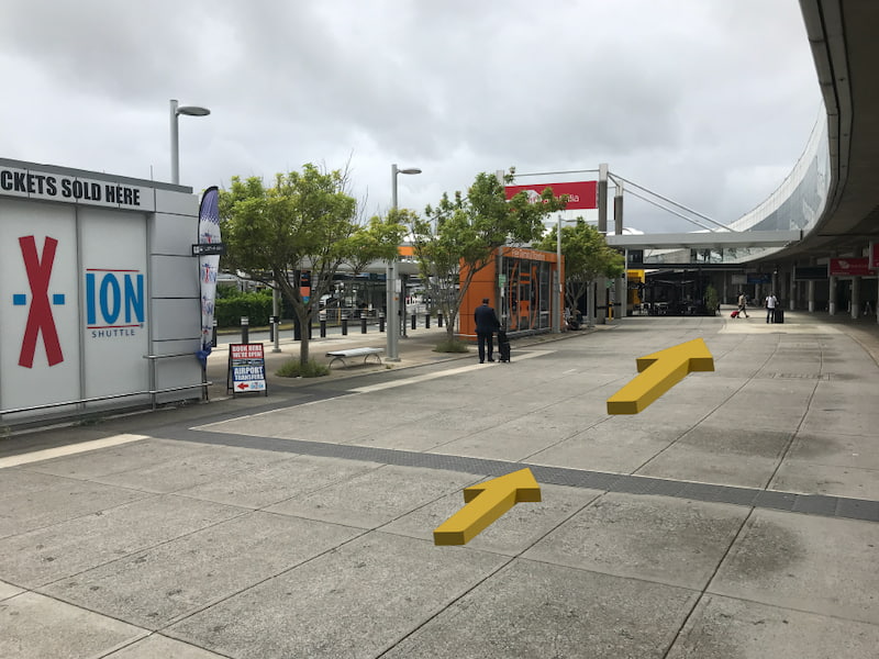 Outdoor side walk. On the right is Brisbane Airport on the left is a shuttle bus kioski