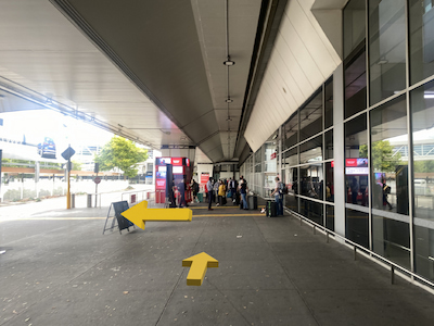 Sidewalk next to airport with people waiting in the distance.